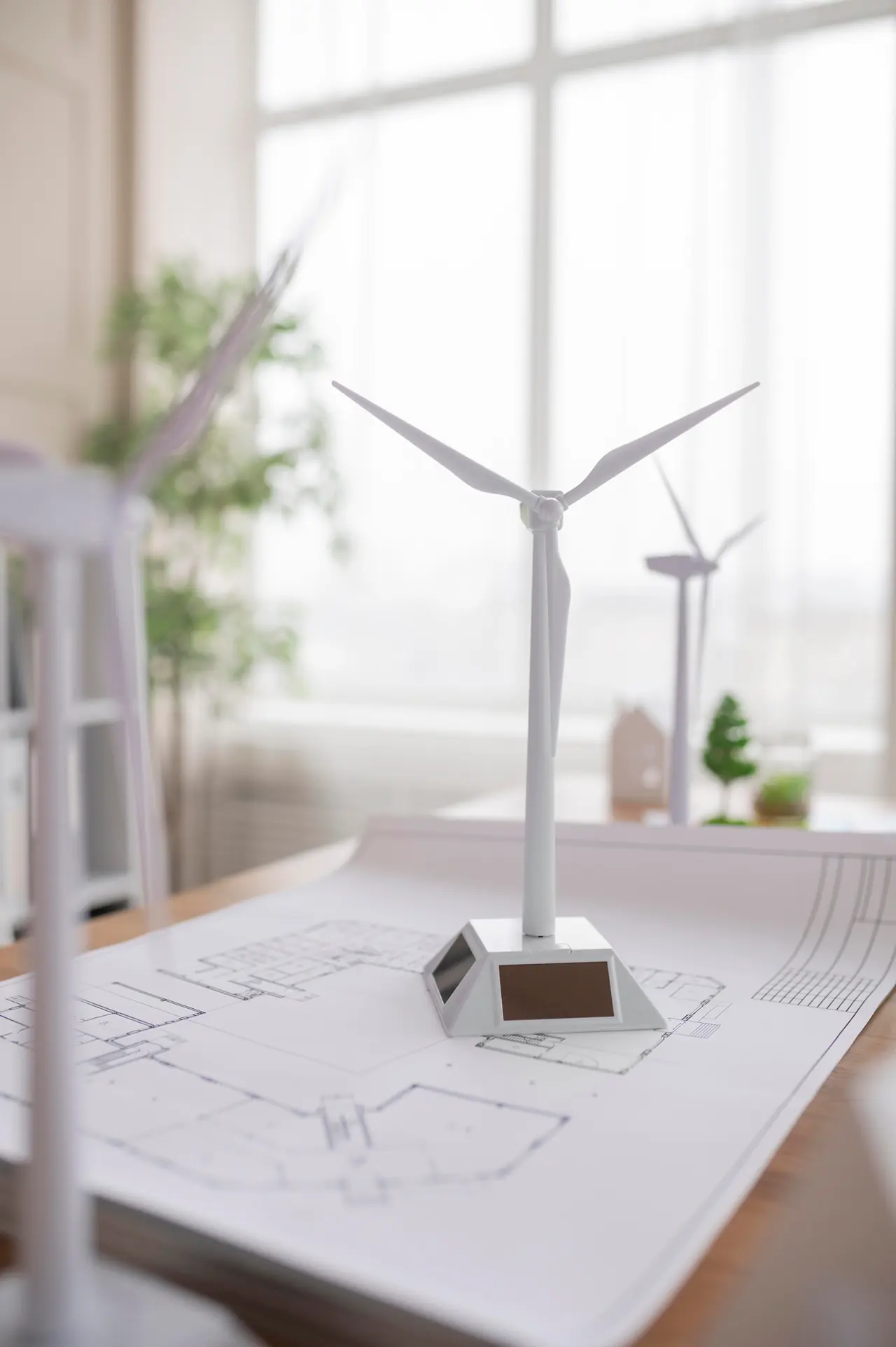 White model wind turbine standing on architectural floor plans on a desk in a bright, softly lit office