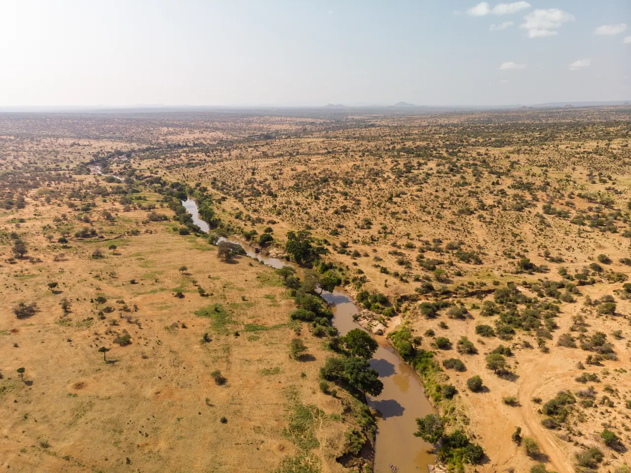 Aerial view of a muddy river winding through dry, bush-dotted savanna towards a hazy horizon